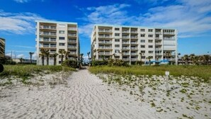 A pathway leading to two multi-story buildings with balconies, surrounded by sand and sparse vegetation. - Paradise Sea's:  Updated 2B/2B with Ocean View (Cocoa Beach)