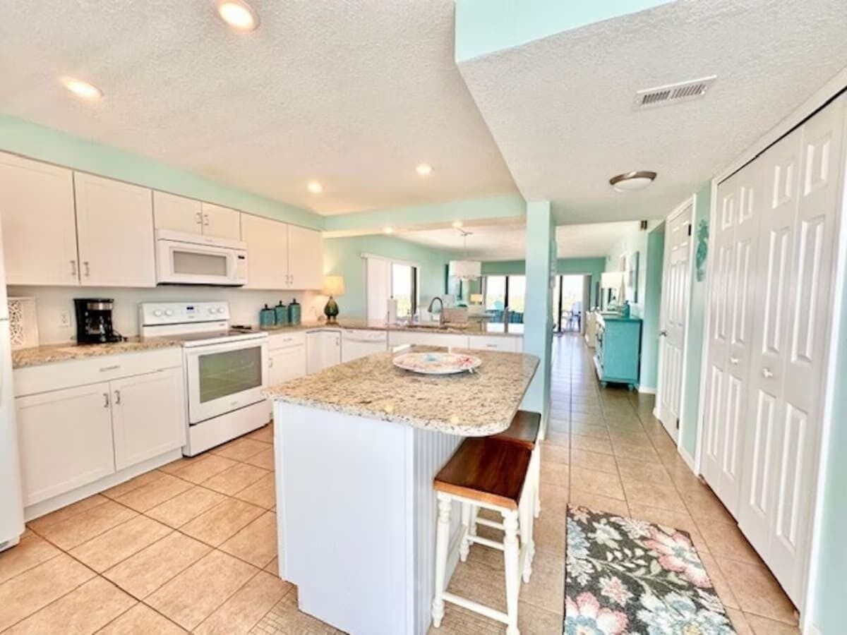 A spacious kitchen with white cabinets, a granite countertop, and a central island with a bench.