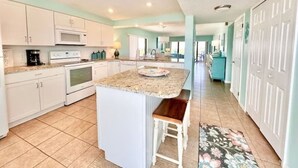 A spacious kitchen with white cabinets, a granite countertop, and a central island with a bench. - Paradise Sea's:  Updated 2B/2B with Ocean View (Cocoa Beach)