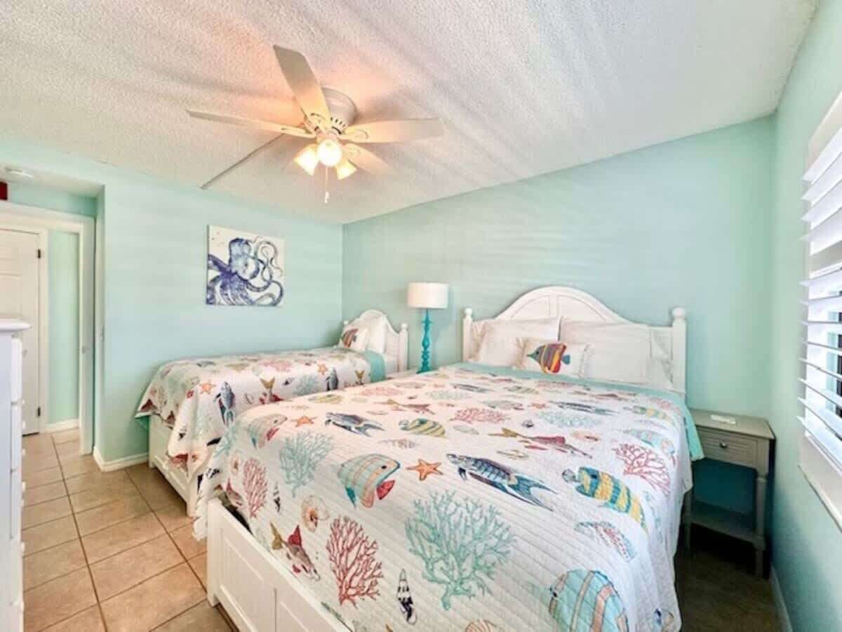 A bedroom with two beds, a ceiling fan, and a wall painting.