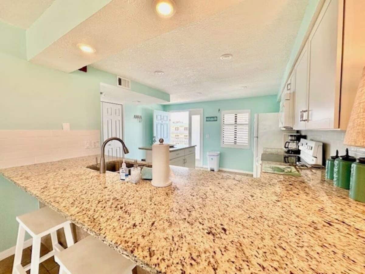 A kitchen with granite countertops, a sink, and a white stool.