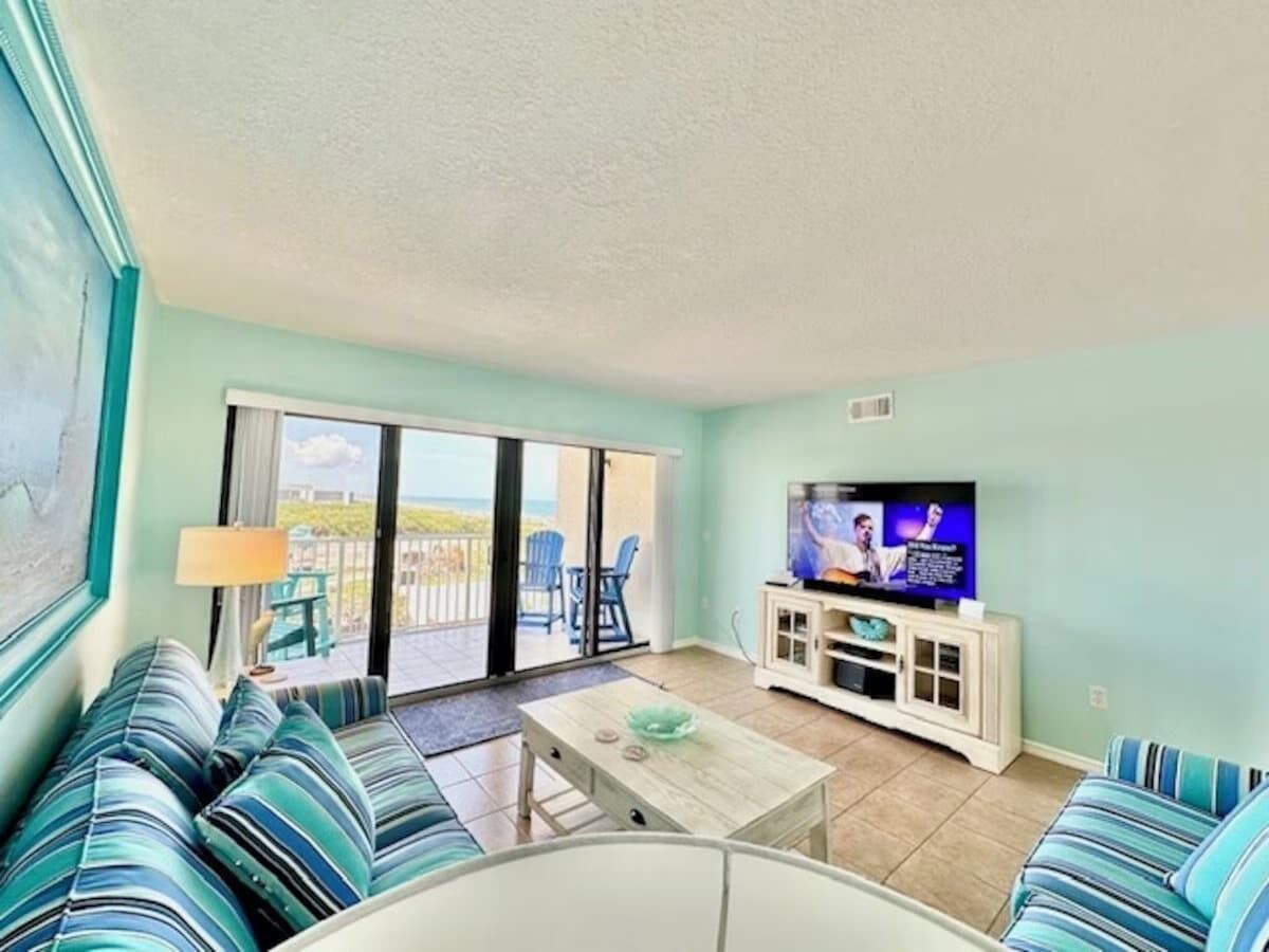 A living room with a sofa set, a coffee table, a television, and a sliding glass door leading to a balcony.