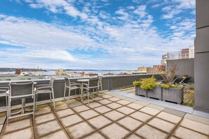 A rooftop terrace with a view of the city skyline, outdoor seating, and planters with greenery. - Modern Condo, Gym, Pool, Parking & Balcony Views! (Seattle)
