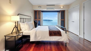 Quarto com cama, mesa de cabeceira, abajur e vista para o mar.