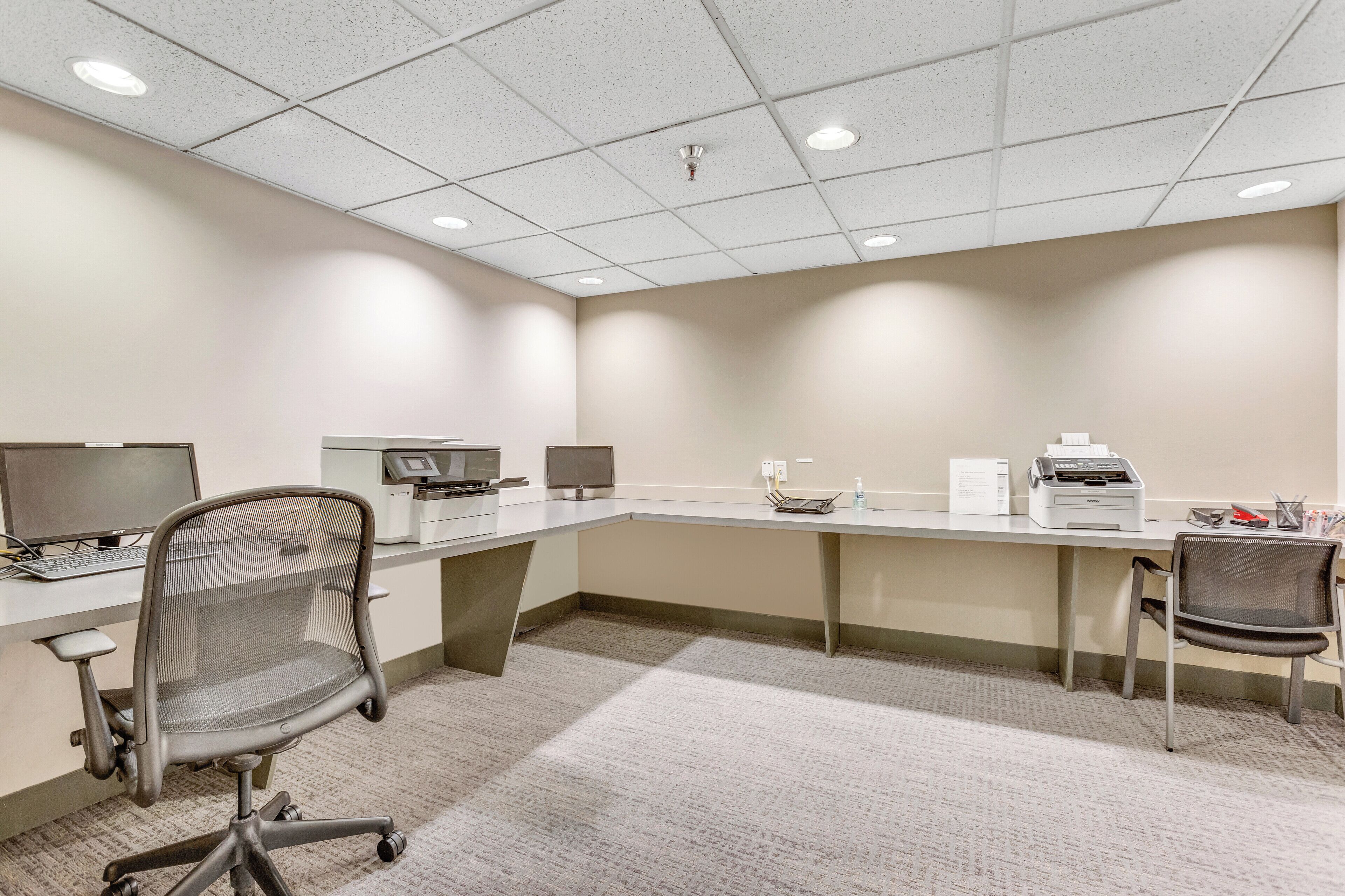 A conference room with a long table, two computers, a printer, and two office chairs.