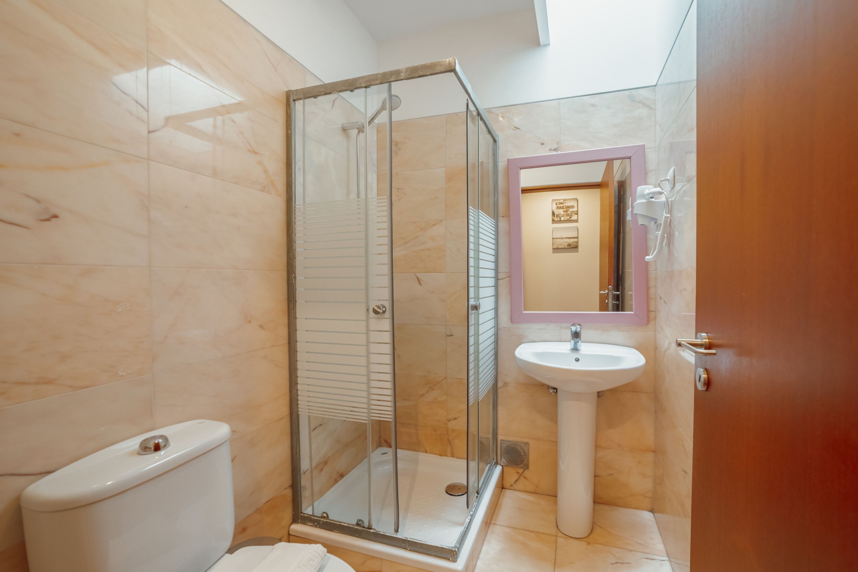 A bathroom with a glass-enclosed shower, a pedestal sink, and a toilet.