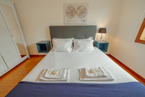 Una cama bien hecha con sábanas blancas y dos toallas, un cabecero gris, una obra de arte con un mapa del mundo y una lámpara de noche.