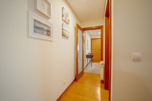 Un pasillo con cuadros en la pared, suelo de madera y una puerta que da a otra habitación.
