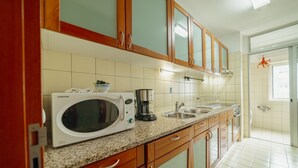 Una cocina con armarios de madera, microondas, cafetera y lavamanos.