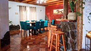 Un espace repas avec des tables et des chaises en bois, un mur décoratif en pierre et une plante suspendue.