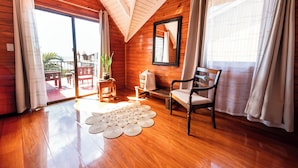 L’intérieur d’un chalet en bois est doté d’un plafond en bois, d’une grande porte-fenêtre coulissante donnant sur un espace extérieur, d’un banc en bois, d’une chaise et d’un tapis tissé sur le sol.