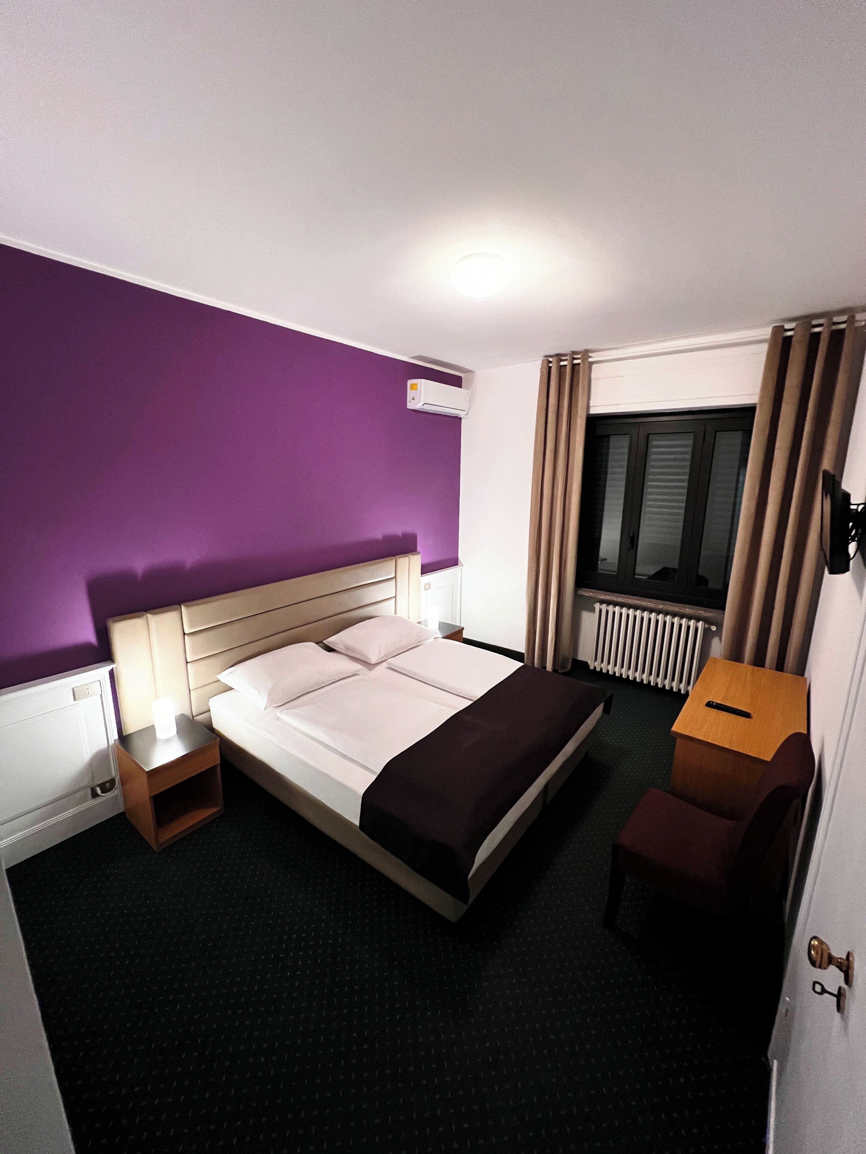 Ein Hotelzimmer mit Bett, Nachttisch, Lampe und kleinem Holztisch.