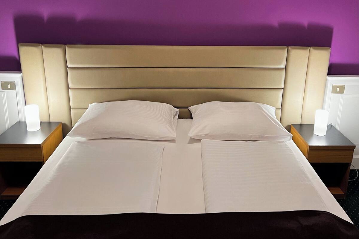 Una cama con cabecera, dos mesitas de noche y una pared morada.