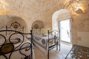 A stone-walled room with two beds, a table, and a window with curtains.