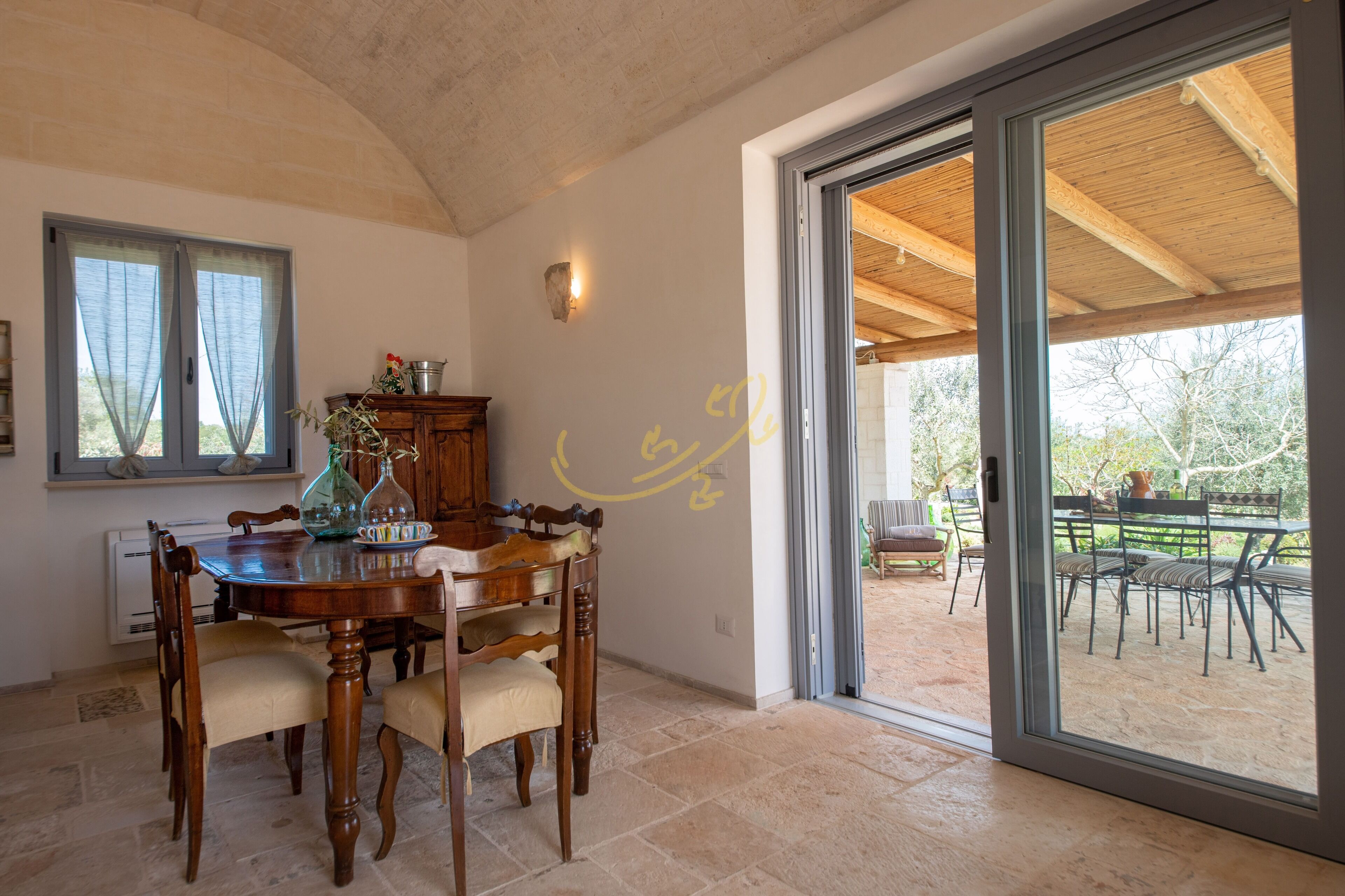 A dining area with a wooden table and chairs, a window with curtains, and a view of an outdoor patio.