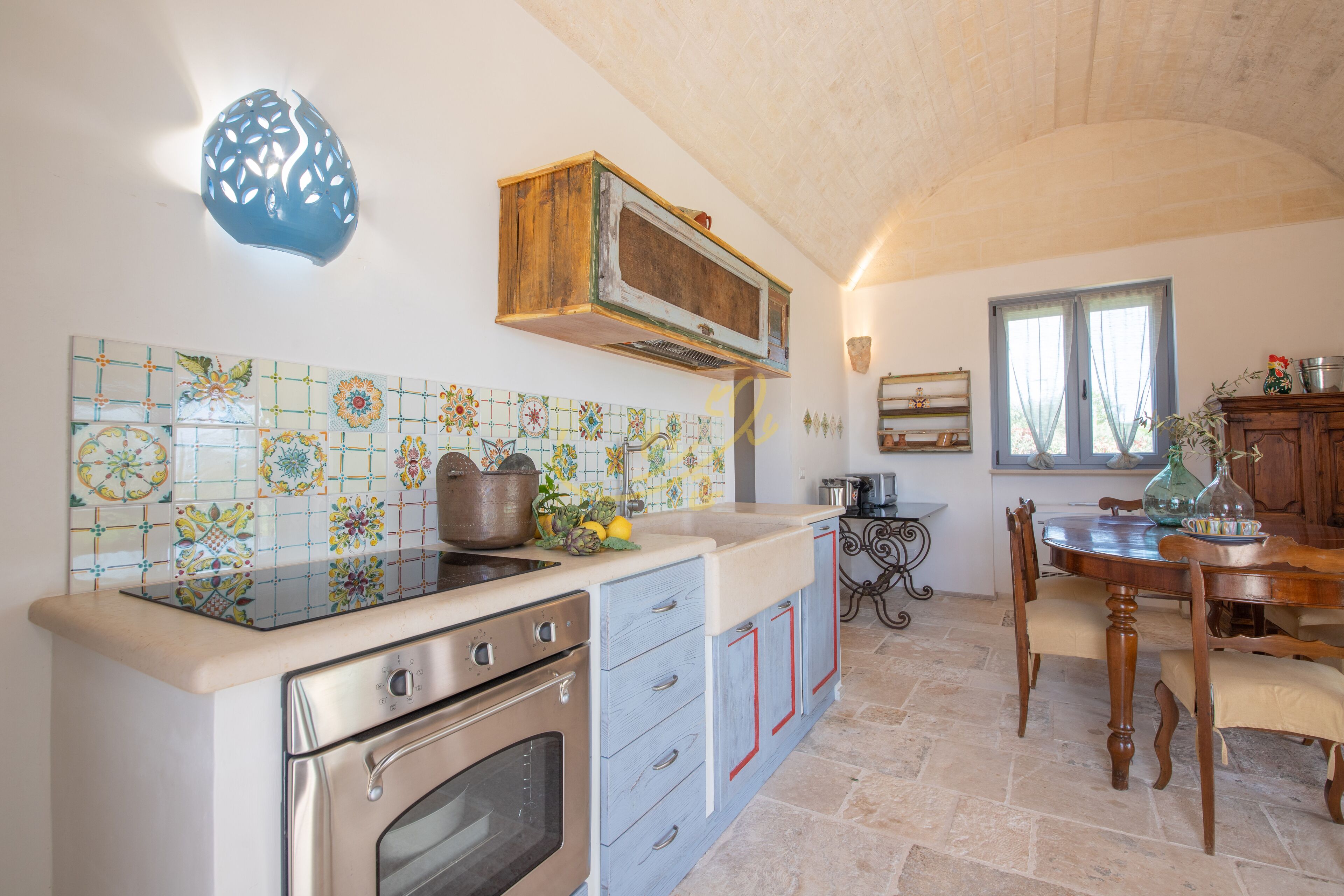 A kitchen with a tiled backsplash, a wooden cabinet, a stove, and a dining area with a table and chairs.