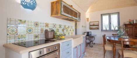 A kitchen with a tiled backsplash, a wooden cabinet, a stove, and a dining area with a table and chairs.
