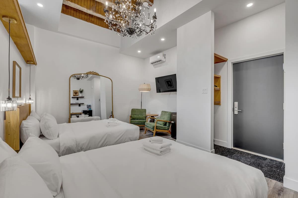 A hotel room with two beds, a chandelier, a mirror, a television, and a door leading to a hallway.