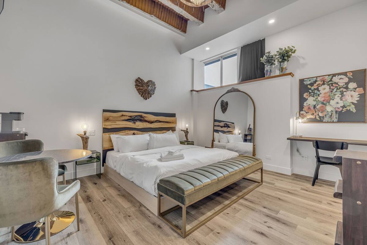 A modern bedroom with a wooden headboard, a bedside table, a bench, a desk, and a chair.