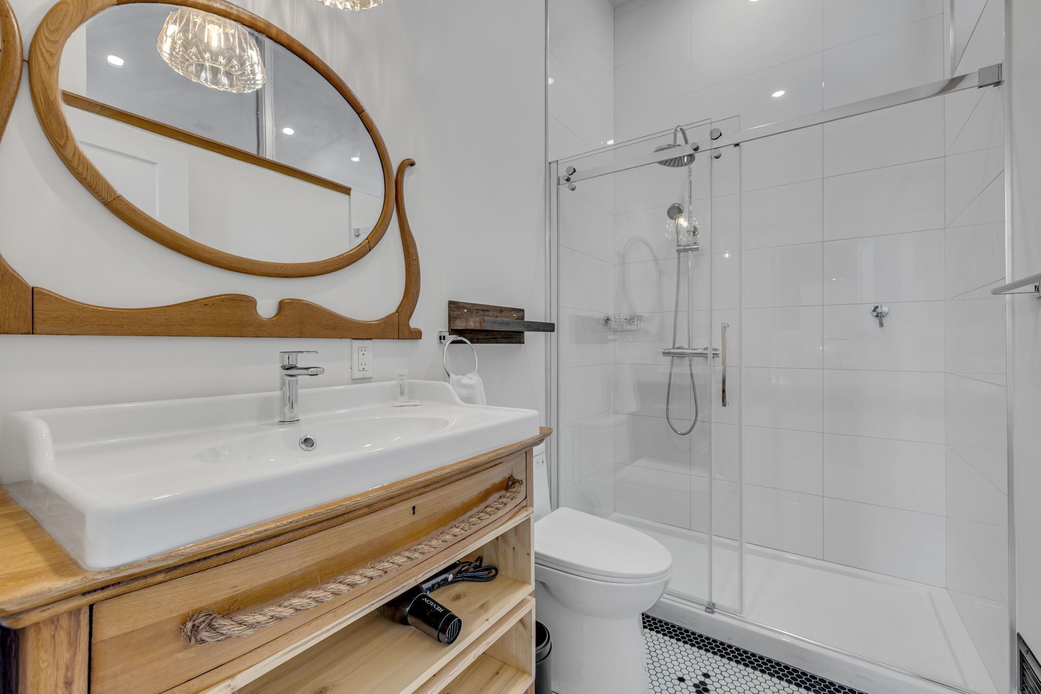 Un baño con tocador de madera, un espejo grande, un lavabo blanco, un inodoro y una ducha con cerramiento de vidrio.