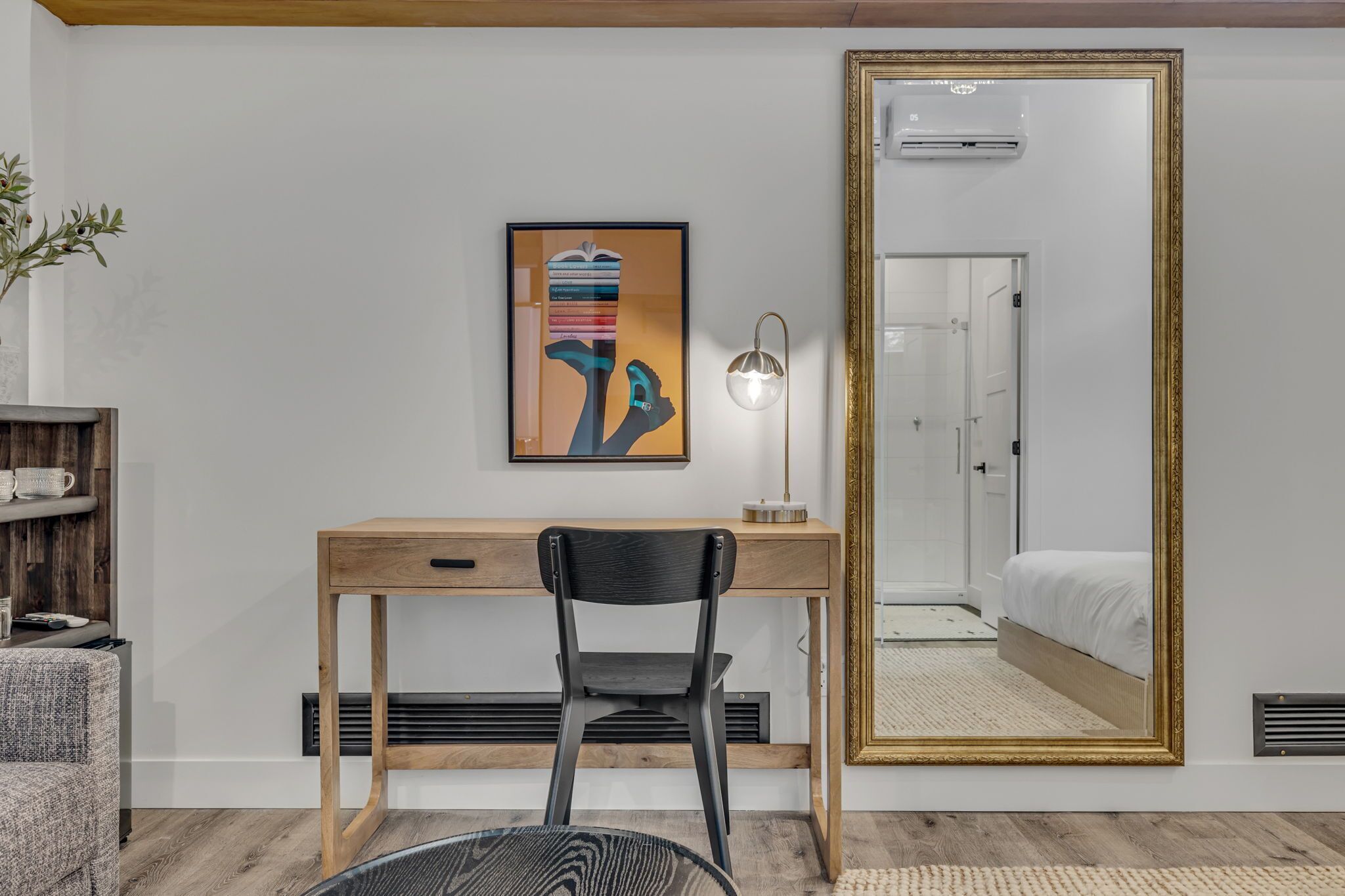 Un dormitorio con un espejo grande, un escritorio con silla, una cama y un aire acondicionado instalado en la pared.