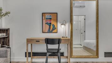 Un dormitorio con un espejo grande, un escritorio con silla, una cama y un aire acondicionado instalado en la pared.
