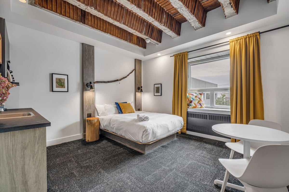 A modern hotel room with a bed, a small table, and a window with curtains.