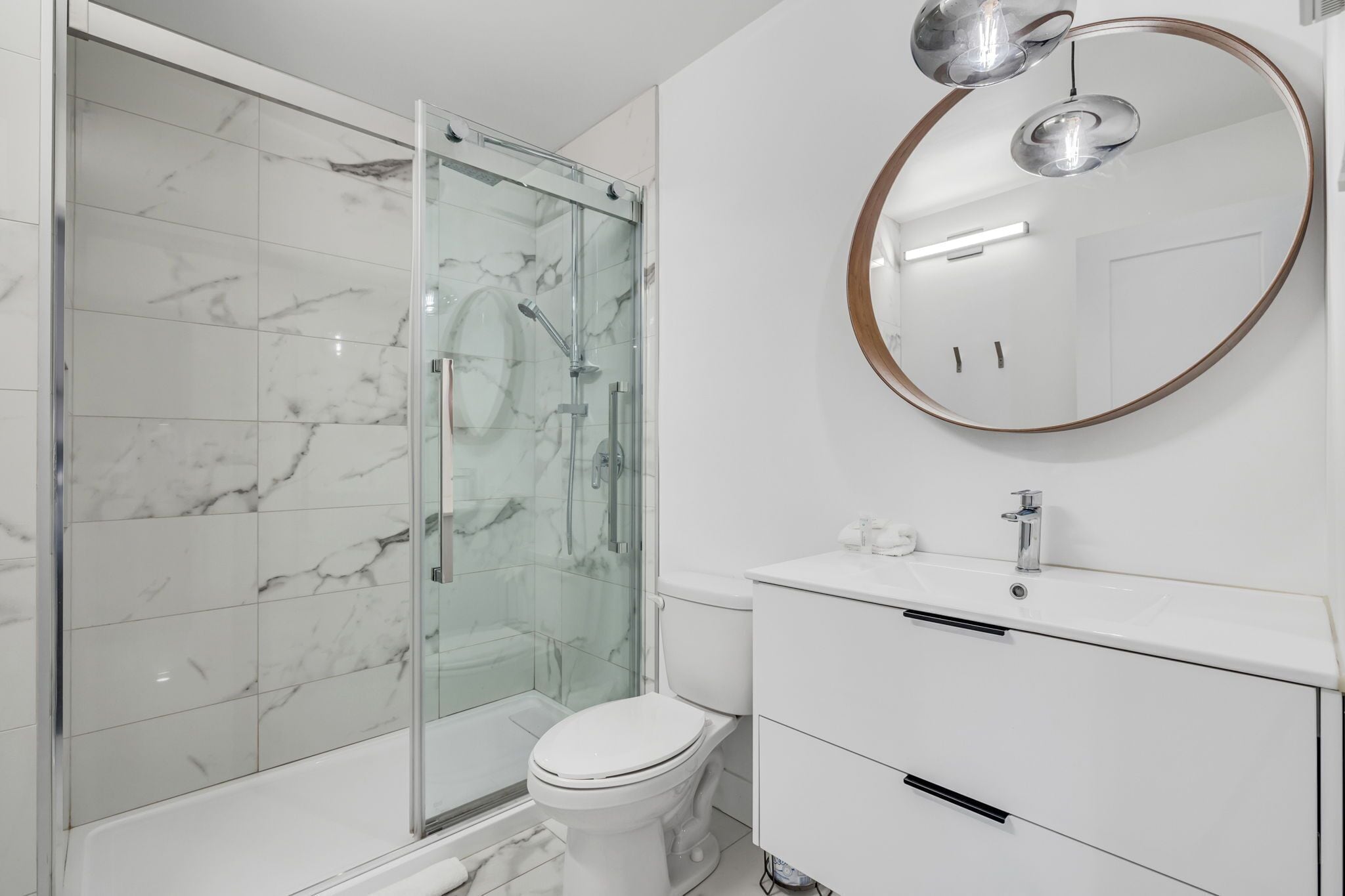 A modern bathroom with a glass-enclosed shower, a white toilet, and a vanity with a mirror.