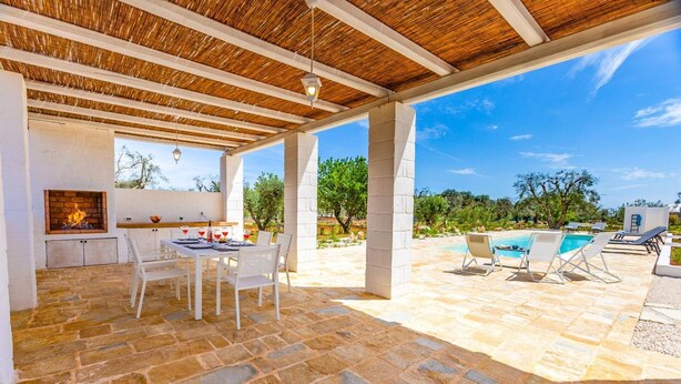 Eine Terrasse im Freien mit Steinboden, weißer Möbel, einer Feuerstelle und einem Poolbereich.