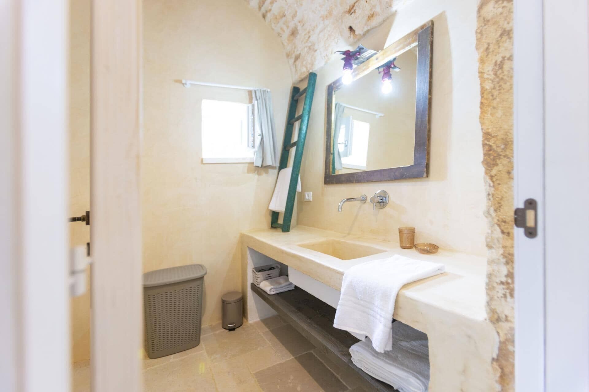 Ein Badezimmer mit Steinwand, Waschbecken, Spiegel, Handtuchhalter und Mülleimer.