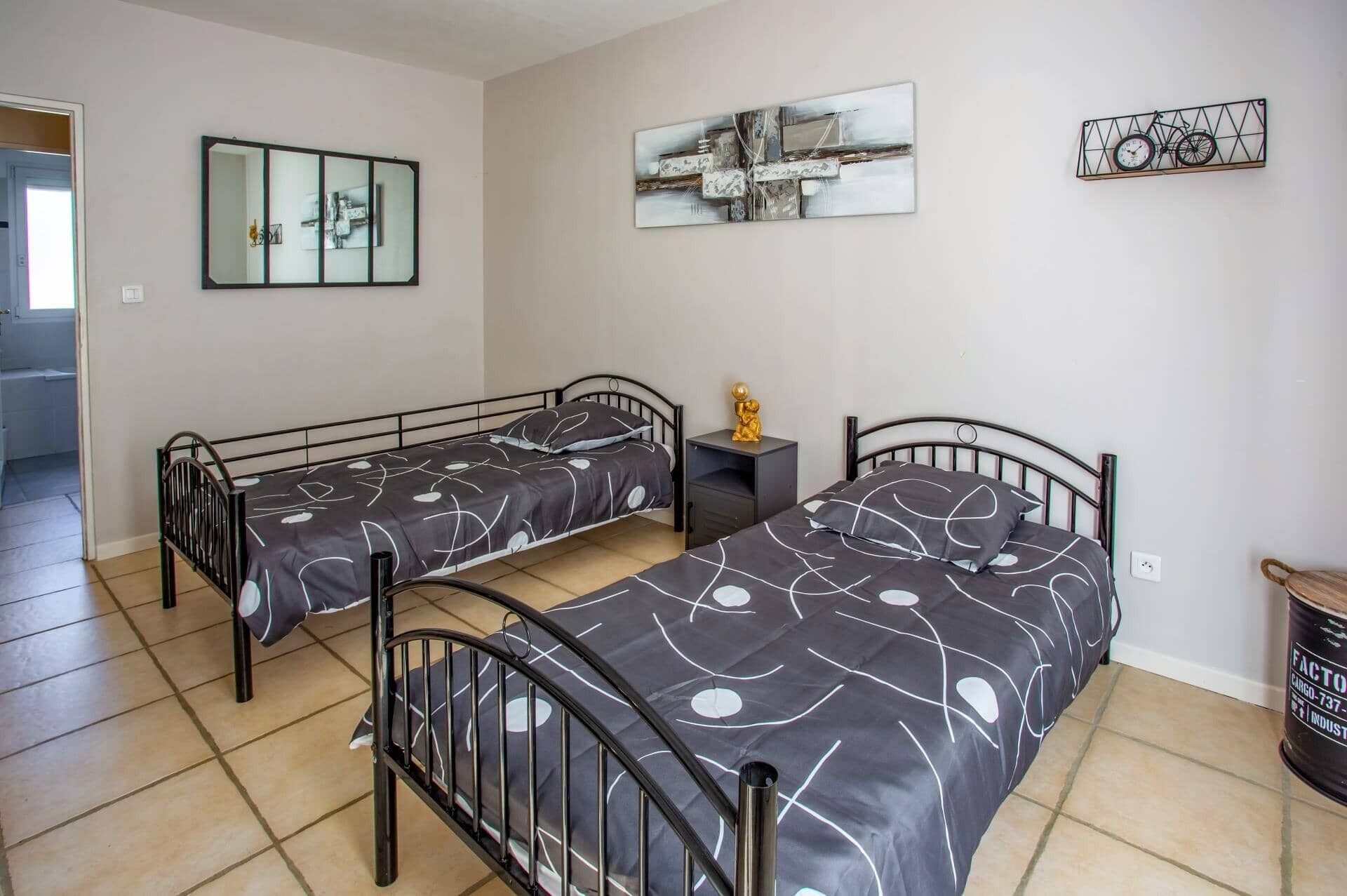 Ein Zimmer mit zwei Betten, einem kleinen Tisch und Bildern an den Wänden.