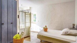 Un dormitorio con cama, mesita de noche, lámpara, una cesta de mimbre con toallas y un armario.