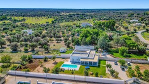 A modern house with a swimming pool, surrounded by a large garden and a view of the countryside.