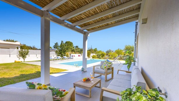 A covered outdoor area with a pool, lounge chairs, and a table with fruit and drinks.