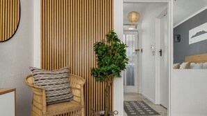 Una habitación con una silla de mimbre, una planta en maceta, un muro de listones de madera y una cama con cabecero.