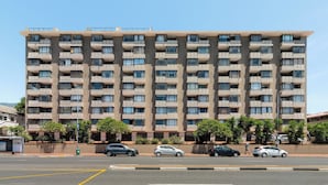 Un edificio residencial de varios pisos con balcones, estacionamiento y cielo despejado.