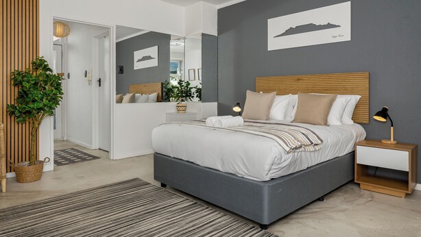 Un dormitorio moderno con una cama grande, mesitas de noche, un espejo y una planta en maceta.