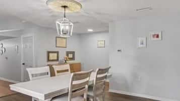 A dining area with a white table and chairs, a chandelier, and framed pictures on the wall.