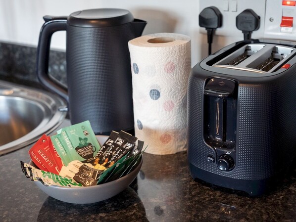 A kitchen counter with a coffee maker, a roll of paper towels, a toaster, and a bowl of coffee packets.