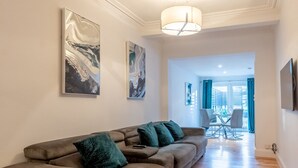 A modern living room with a grey sofa, two abstract paintings, a hanging light fixture, and a view into the dining area. - Cosy flat in Leigh - Pass the Keys (Southend-on-Sea)