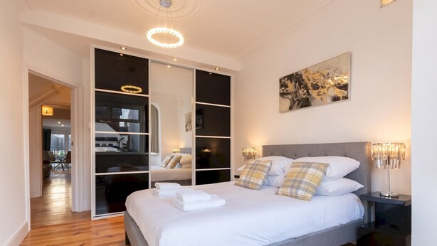 A modern bedroom with a grey bed, white linens, and a large mirror. - Cosy flat in Leigh - Pass the Keys (Southend-on-Sea)