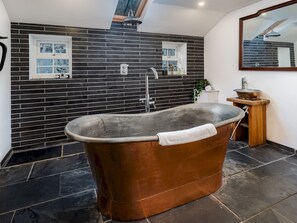 A modern bathroom with a freestanding copper bathtub, a wooden vanity with a copper basin, and a large mirror above the vanity.