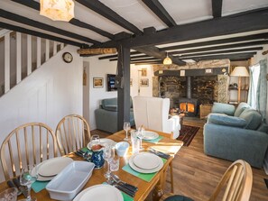 A dining area with a wooden table set for four, a stone fireplace, and a staircase leading to another level. - Cosy cottage hideaway set in beautiful countryside - Pass the Keys (Hopesay)