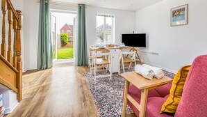 Uma sala de estar moderna com escada de madeira, área de jantar com mesa e cadeiras, TV de tela plana na parede e um tapete colorido.