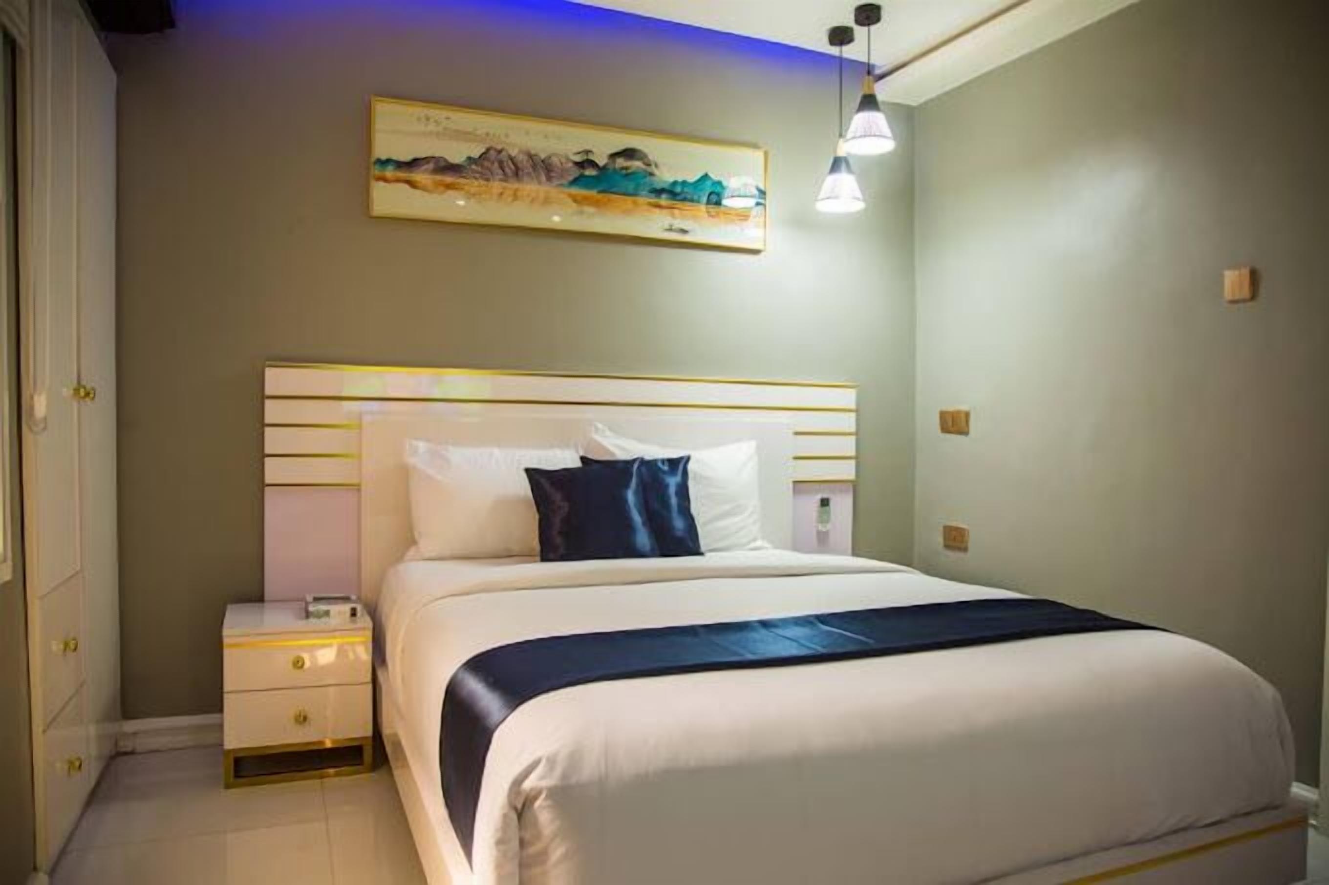 A neatly arranged bedroom with a large bed, bedside tables, and a painting on the wall.