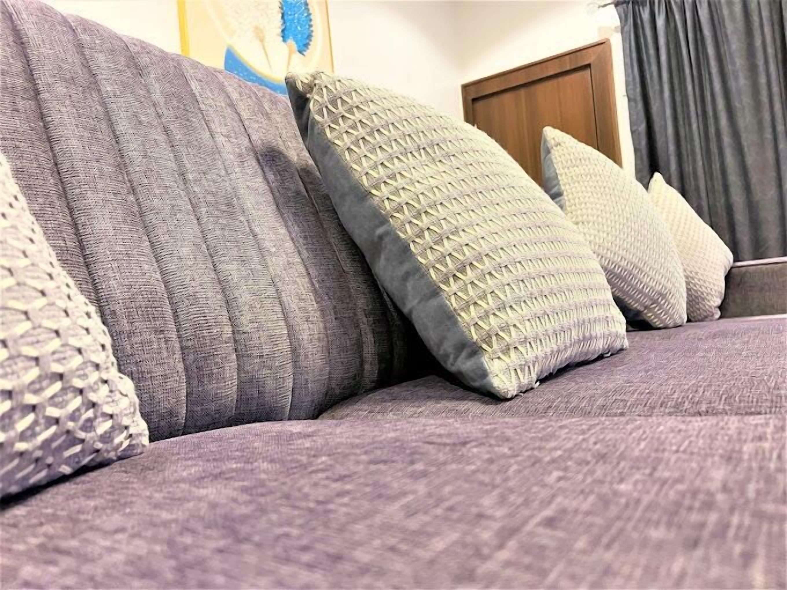 Parte de un sofá con varios cojines, un cabecero de madera y una cortina oscura al fondo.