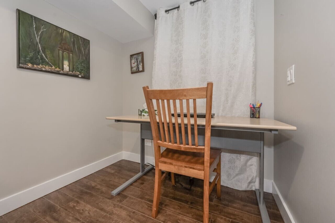 A wooden chair at a desk with a curtain and a painting on the wall.