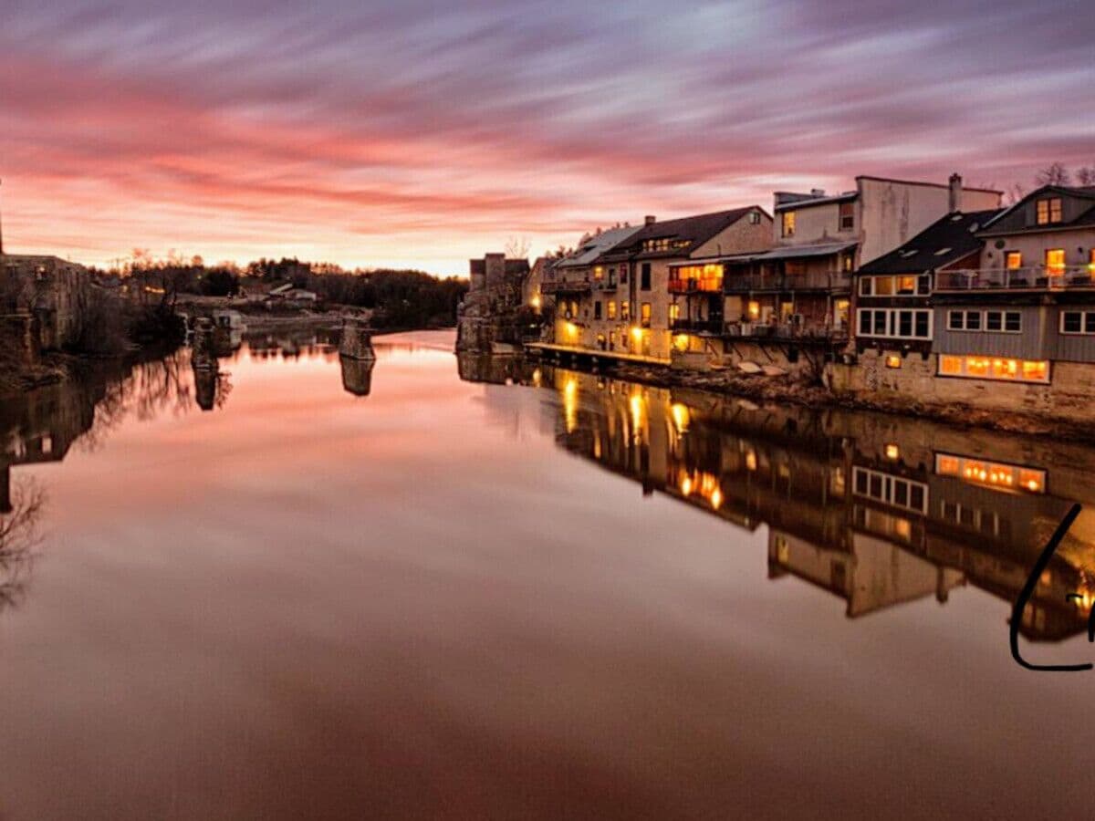 Een plaats aan de rivier met gebouwen die in het water weerspiegelen, een brug en een zonsondergang.