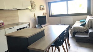 A modern kitchen with a dining area, a large window, and a flat-screen TV.