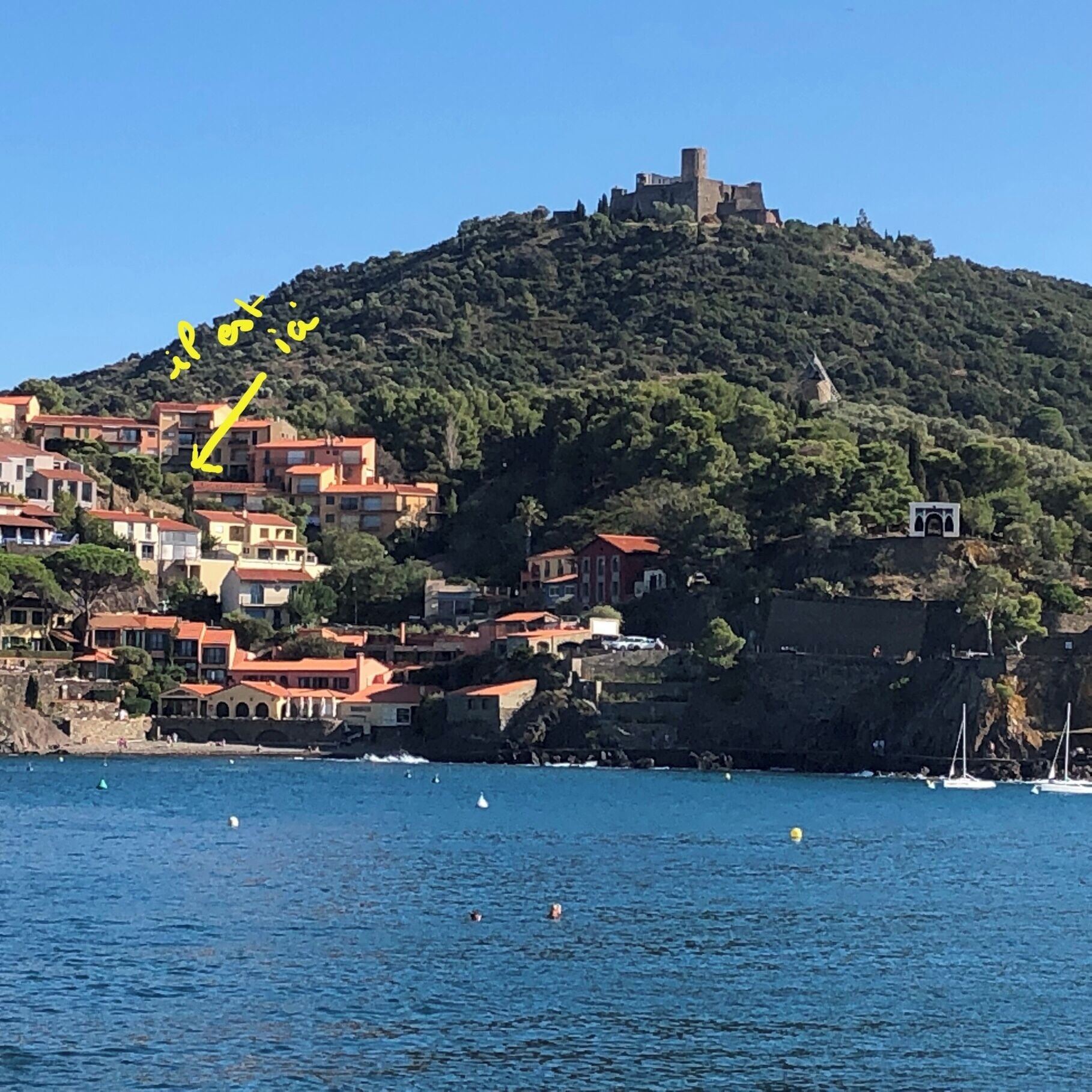 A coastal town with buildings on a hillside, a castle on top, and boats in the water.